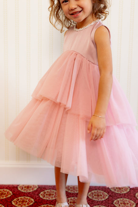 Close up of a little girl in a pink dress standing against a white wall