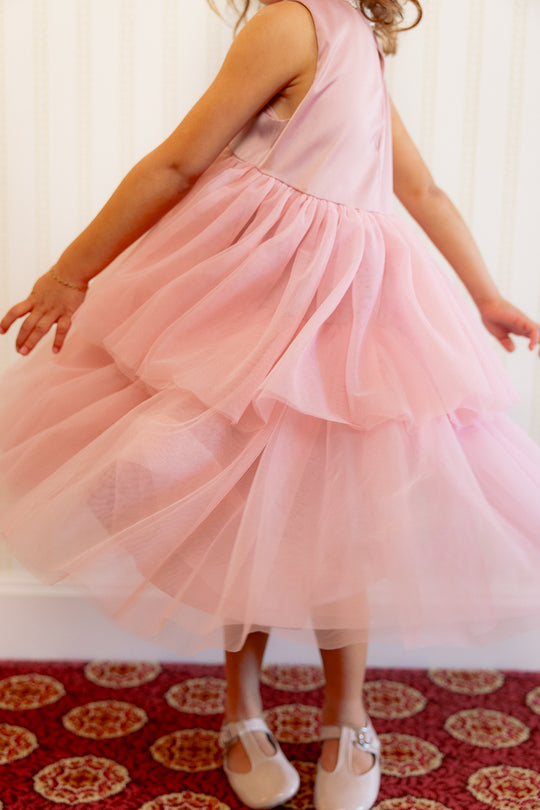 close up of a little girl in a pink dress standing against a white wall