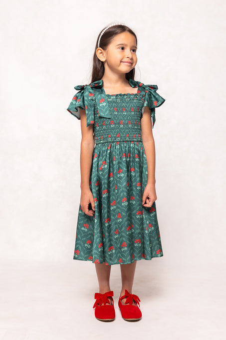 Young girl wearing a green dress with red patterns and red shoes on a white background