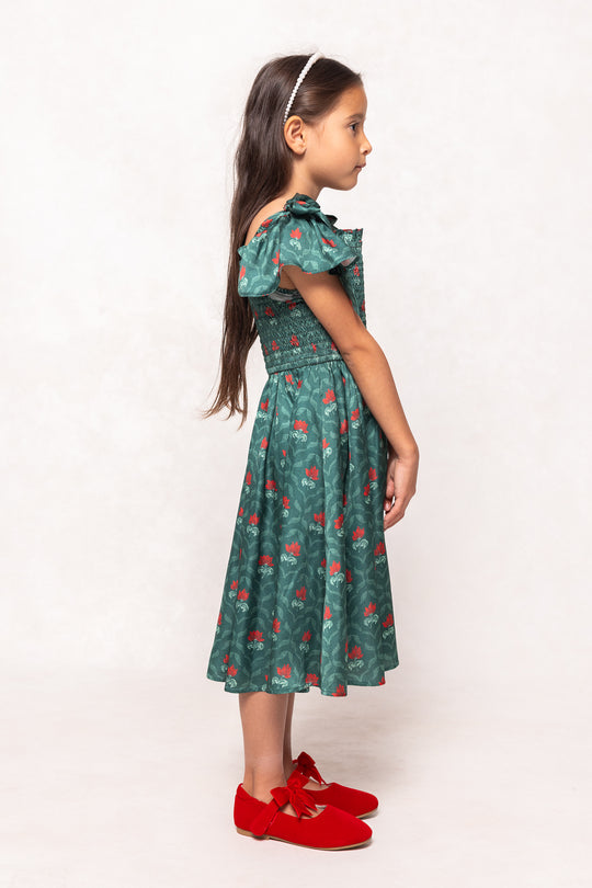 Young girl wearing a green dress with red patterns and red shoes on a white background