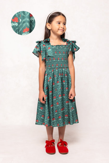 Young girl wearing a green dress with red floral pattern on a white background