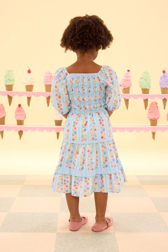 Child wearing a floral dress standing in front of an ice cream cone display.