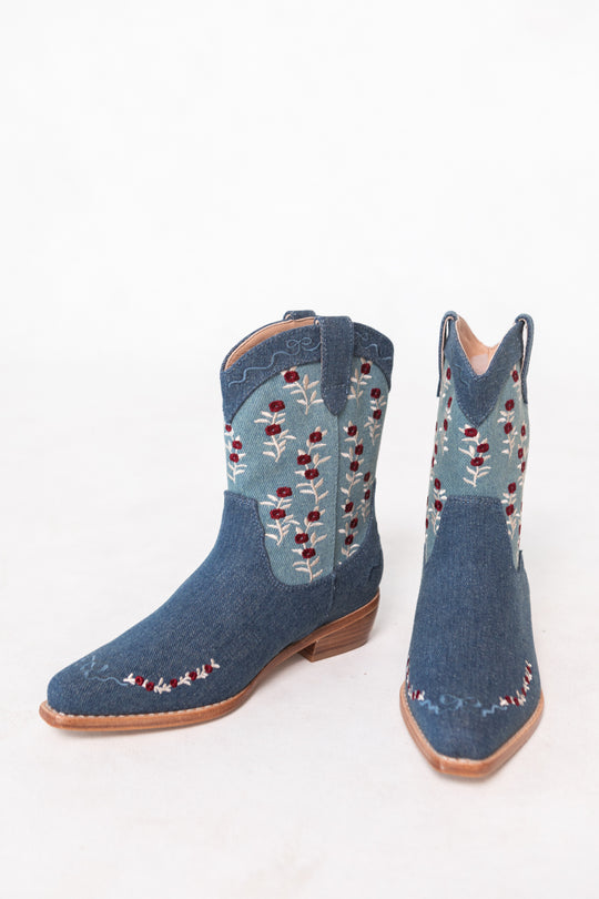 The Mini Rosemary Cowgirl Boots in Denim by Ivy City Co feature red and white floral embroidery on blue denim with wooden heels, stylishly displayed on a light background—perfect for fans of unique, embroidered boots.