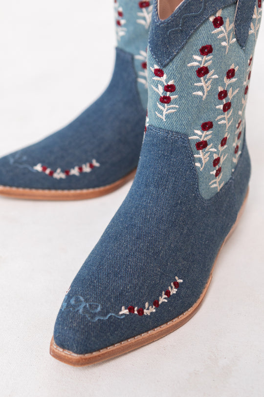 The Mini Rosemary Cowgirl Boots in Denim by Ivy City Co showcase light blue upper panels, red and white floral embroidery, pointed toes, and light tan soles for a charming cowgirl style.