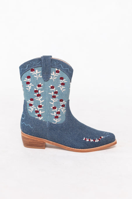 The Mini Rosemary Cowgirl Boots in Denim by Ivy City Co feature white and red floral embroidery, a light brown sole and heel, and pull straps, photographed on a plain white background—ideal for fans of floral embroidered boots.