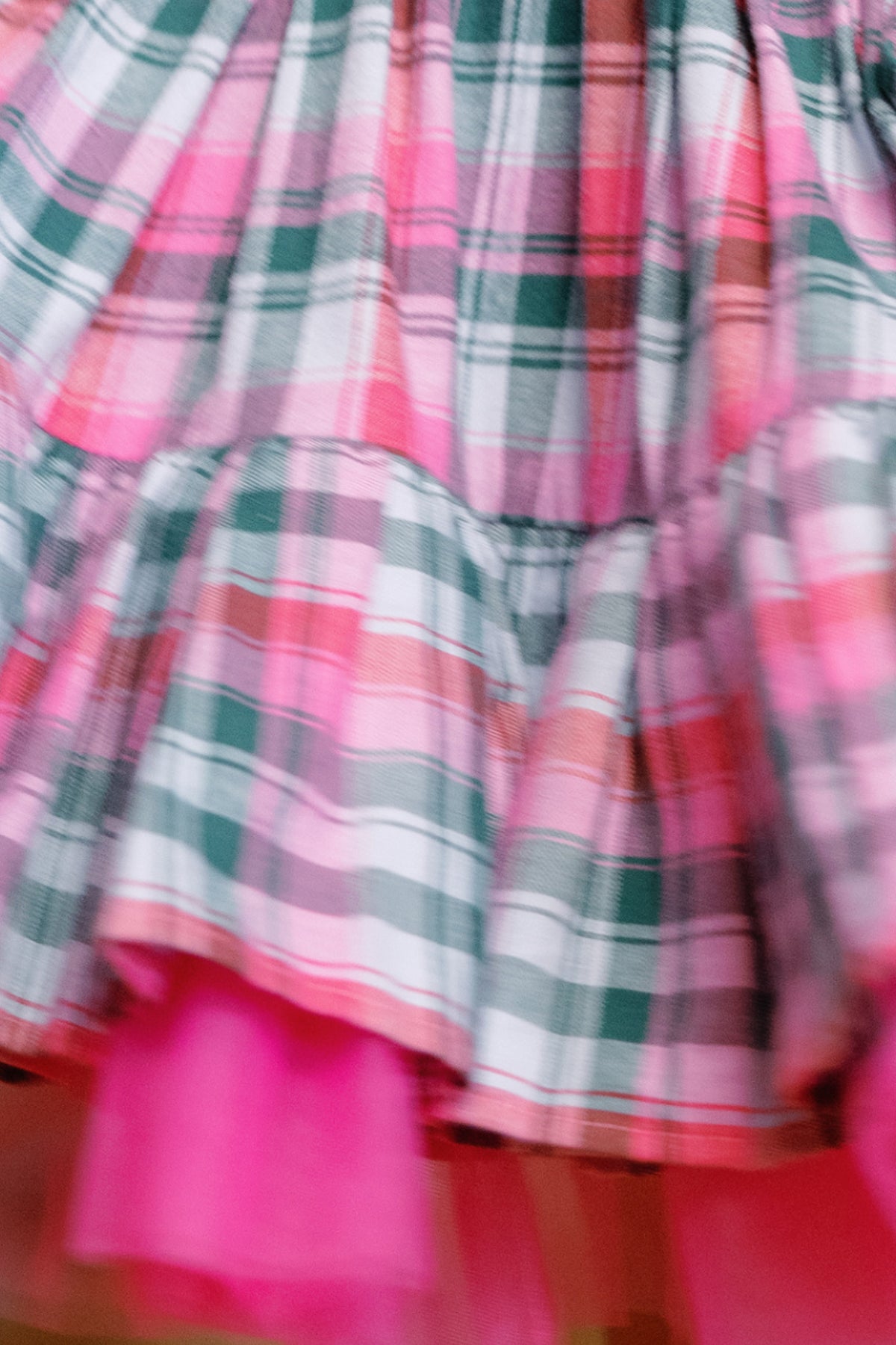 A close-up of the Mini Scottie Dress in Vibrant Plaid by Ivy City Co showcases the ruffled skirt, featuring pink, green, and white plaid layers with soft pink tulle underneath—perfect as a festive holiday party dress for girls.