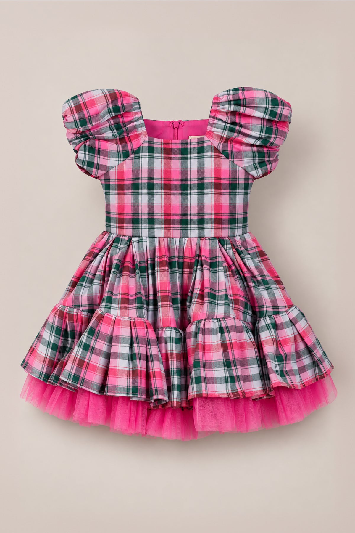 The Mini Scottie Dress in Vibrant Plaid by Ivy City Co features pink, green, and white plaid with puffy short sleeves and a layered tulle skirt—making it a charming girls’ Christmas dress that’s perfect for any holiday party. It is displayed against a plain beige background.