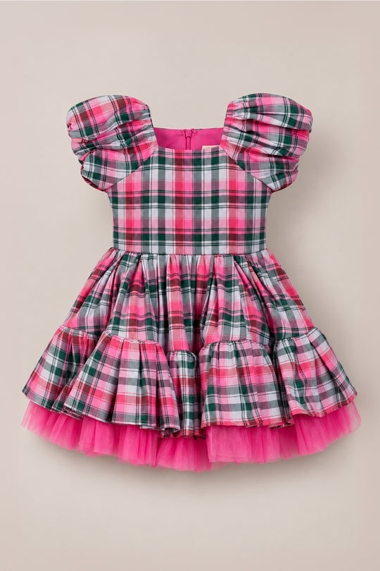 The Mini Scottie Dress in Vibrant Plaid by Ivy City Co features pink, green, and white plaid with puffy short sleeves and a layered tulle skirt—making it a charming girls’ Christmas dress that’s perfect for any holiday party. It is displayed against a plain beige background.