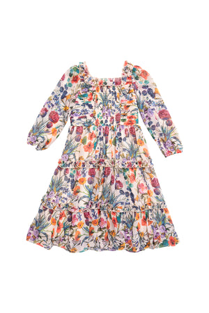 The Mini Selena Dress in Vivid Meadow by Ivy City Co is a girls’ floral midi with a smocked bodice, long sleeves, square neckline, and tiered ruffle skirt. Colorful blooms and ruffles at the shoulders add charm to its lightweight, flowing fabric.