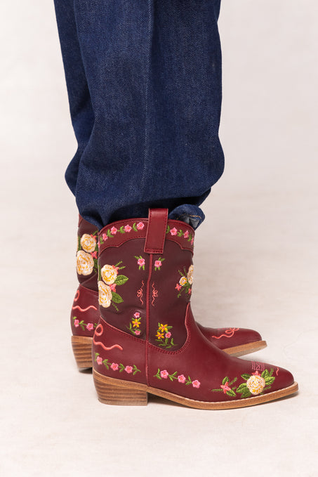 Red cowboy boots with floral embroidery worn with blue jeans on a white background