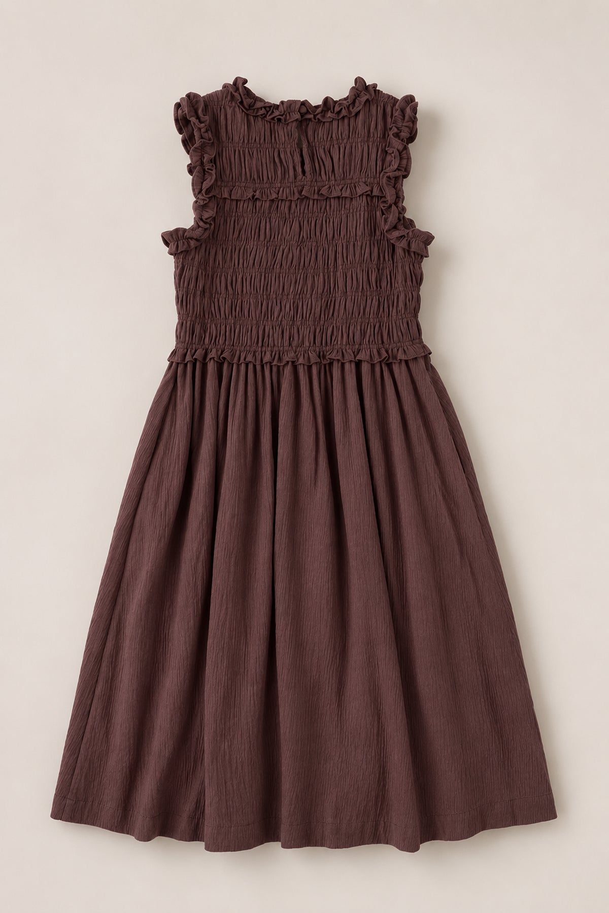 The Ivy City Co Teen Simone Dress in Warm Cocoa, featuring a sleeveless design, smocked bodice, ruffled neckline, practical pockets, and a flowy skirt, is laid flat on a light background.