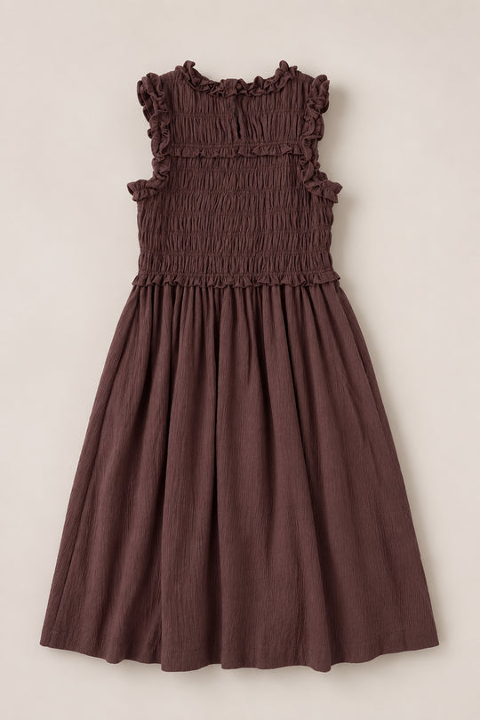 The Ivy City Co Teen Simone Dress in Warm Cocoa, featuring a sleeveless design, smocked bodice, ruffled neckline, practical pockets, and a flowy skirt, is laid flat on a light background.