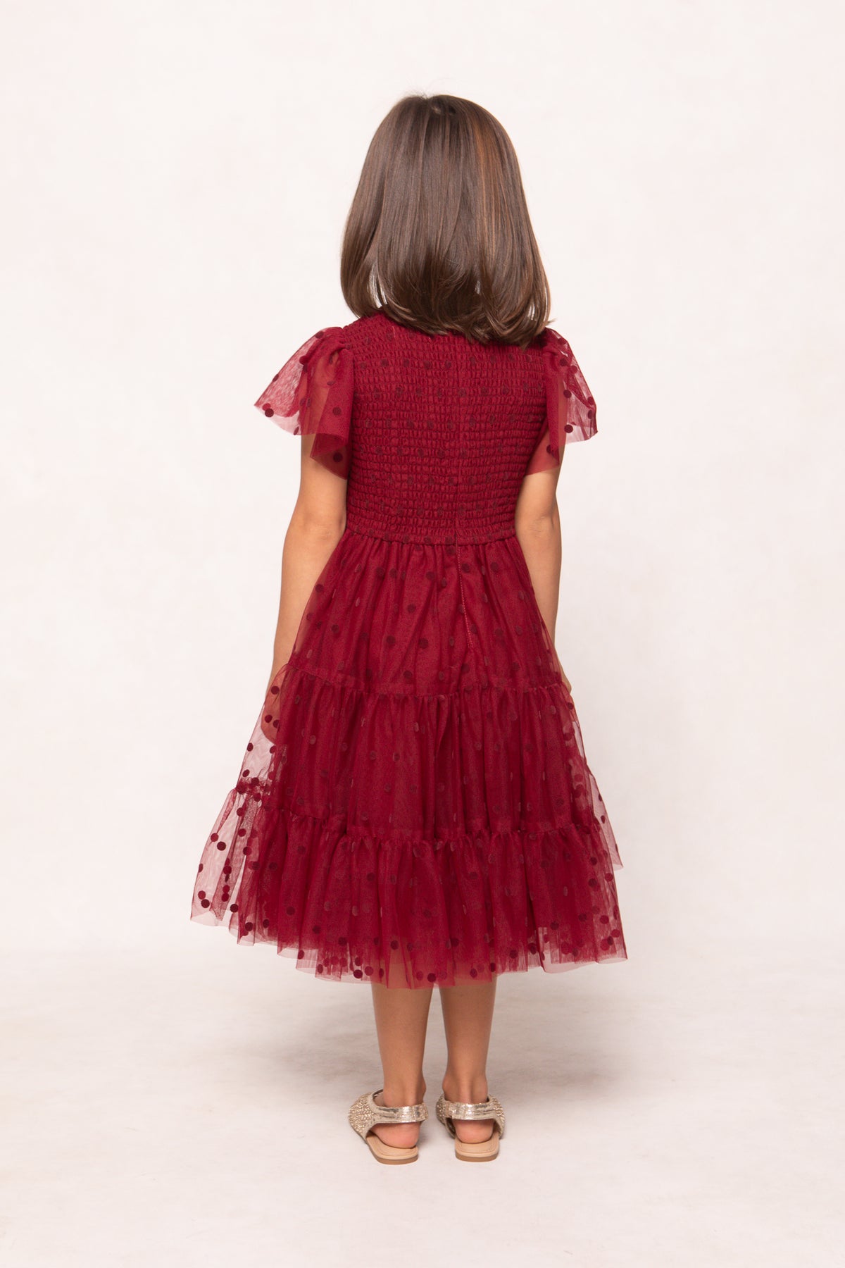 Child wearing a red dress with ruffled sleeves and tiered skirt on a white background