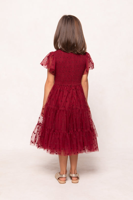 Child wearing a red dress with ruffled sleeves and tiered skirt on a white background