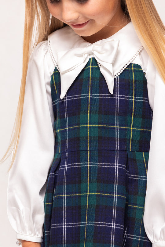 Person wearing a white blouse with a large bow and a green plaid dress.