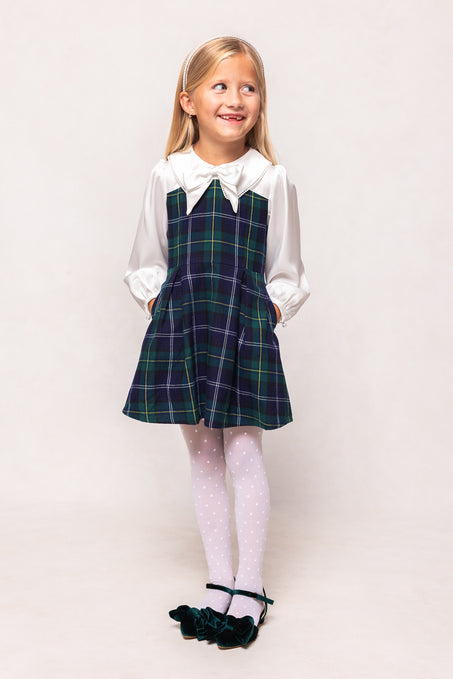 Young girl wearing a plaid dress over a white shirt on a plain background