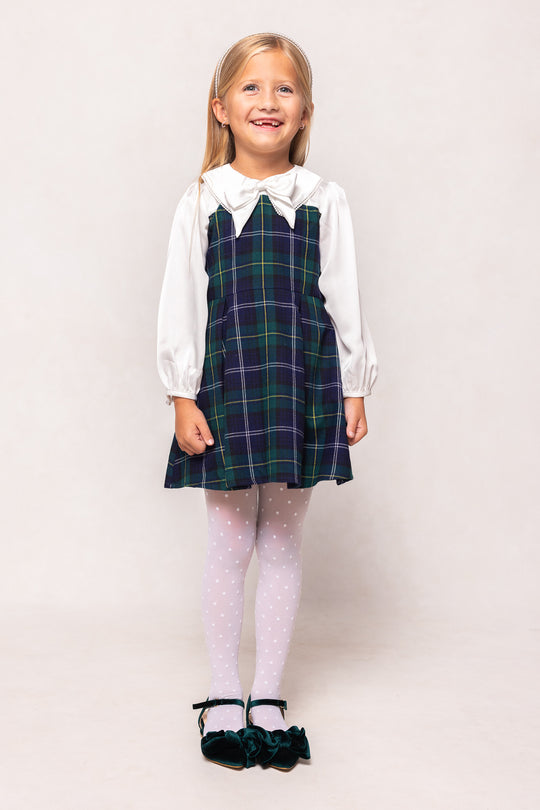 Young girl wearing a plaid dress over a white shirt on a plain background