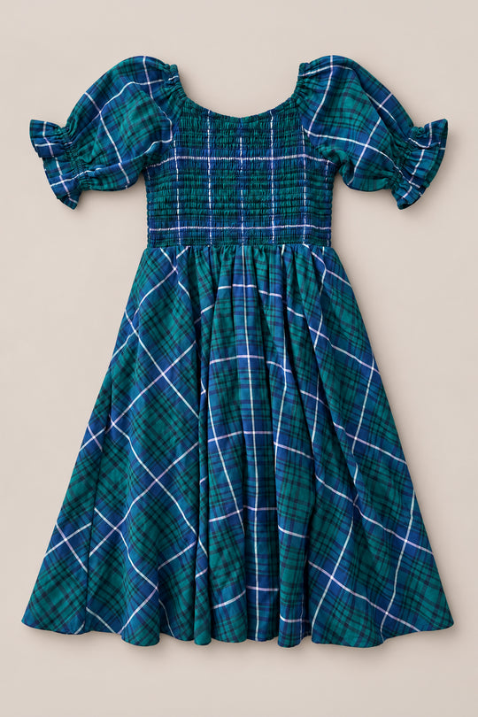 The Mini Teagan Dress in Emerald Plaid by Ivy City Co features a green and blue plaid pattern, short puff sleeves, a smocked bodice, and a flared skirt. Perfect for holiday portraits or as a charming Christmas Eve dress, it is displayed flat on a neutral background.