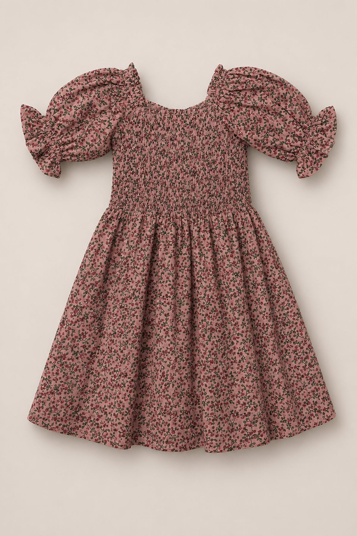 The Mini Teagan Dress in Mauve Woodland Floral by Ivy City Co is a pink cotton dress with short puffed sleeves finished with ruffled ends. Featuring a small floral print, the dress has a square neckline, smocked bodice, gathered waist, and an A-line skirt, all set against a plain light beige background.