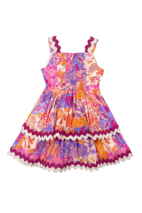 The Mini Tessa Dress in Pink Floral Tile by Ivy City Co is a sleeveless cotton knee-length dress for girls, featuring a colorful pink pattern, gathered elastic bodice, and wavy trim on the straps, waist, and hem.
