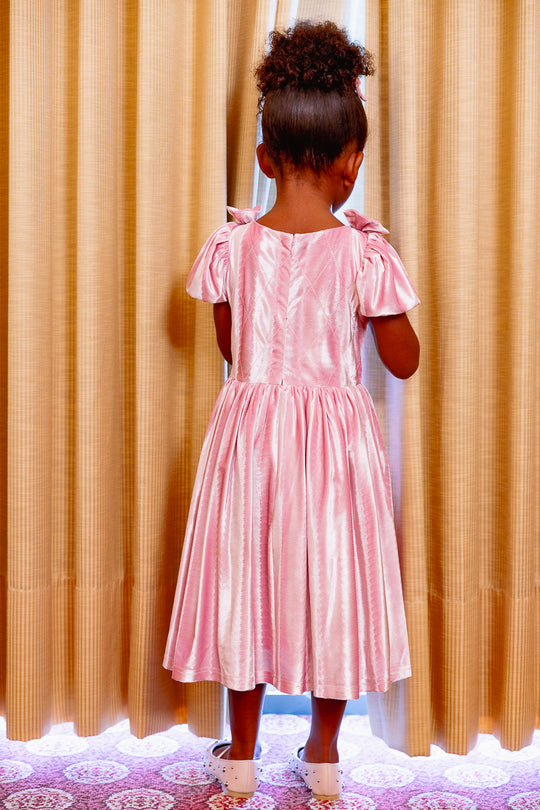 Child wearing a pink dress standing in front of beige curtains