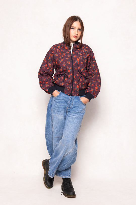 Person wearing a patterned jacket, blue jeans, and black boots on a white background