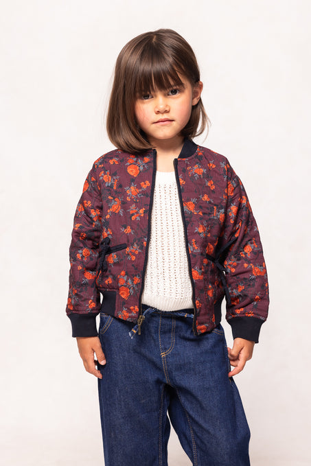 Child wearing a floral bomber jacket and blue jeans on a white background