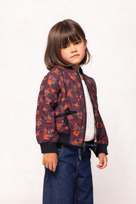 Child wearing a floral bomber jacket on a white background