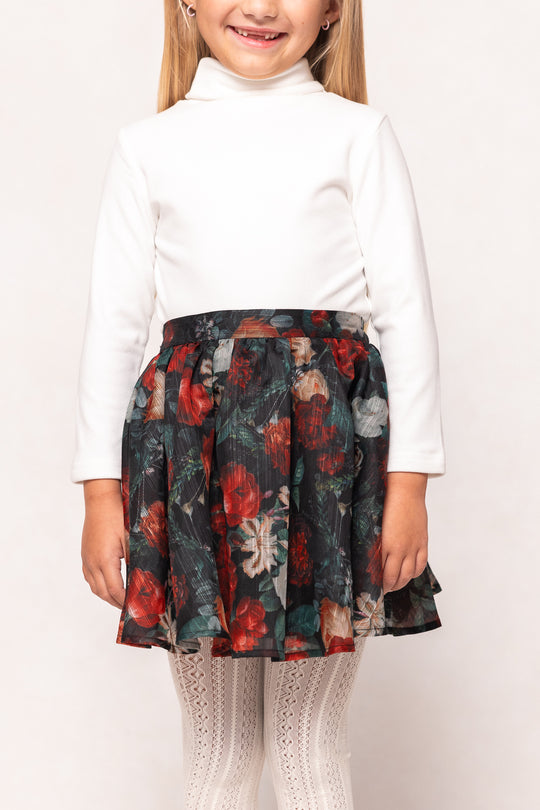 Child wearing a white top and floral skirt on a plain background