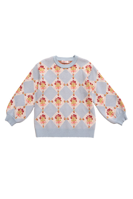 The Mini Vivienne Sweater in Mosaic Bloom by Ivy City Co is a baby blue girls’ sweater with an all-over diamond pattern, red and yellow floral bouquets, ribbed cuffs, hem, neckline, and slightly puffed sleeves.