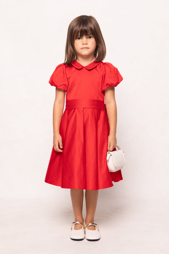 Young girl wearing a red dress with ruffled sleeves on a white background