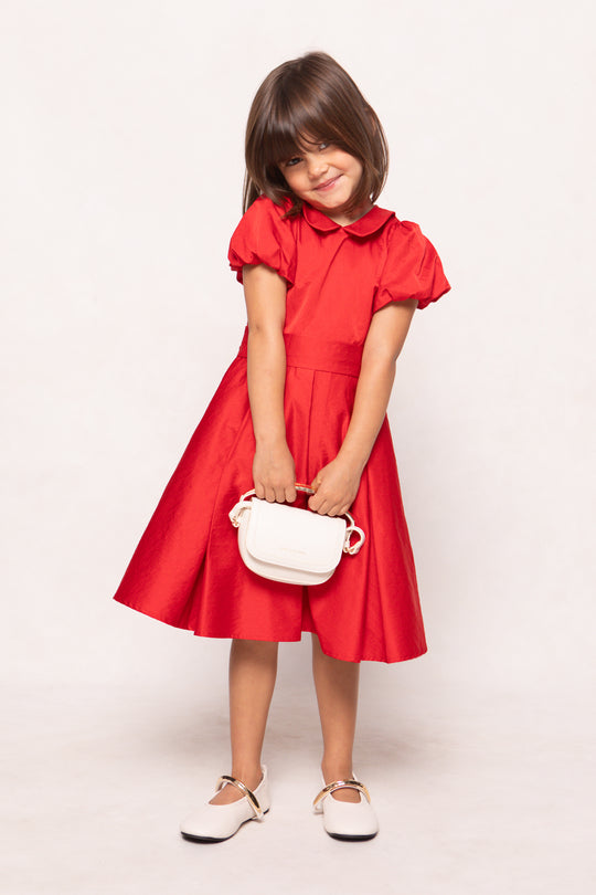 Young girl in a red dress holding a white bag against a light background