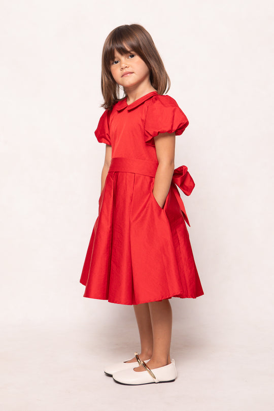 Young girl wearing a red dress with ruffled sleeves and a bow on a white background