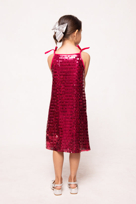 Young girl wearing a red sequin dress with bow straps on a white background