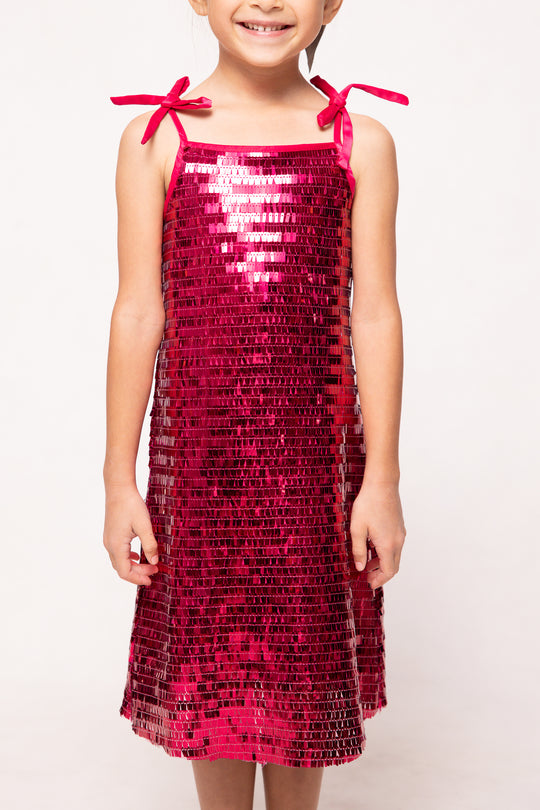 Child wearing a red sequin dress with bow straps on a white background