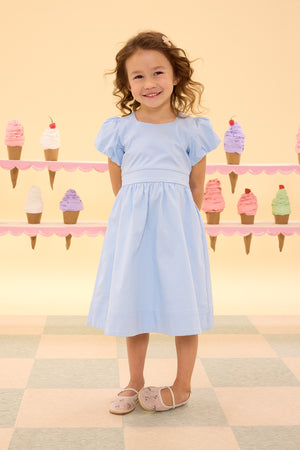 Young girl in a light blue dress standing in front of an ice cream-themed wall.