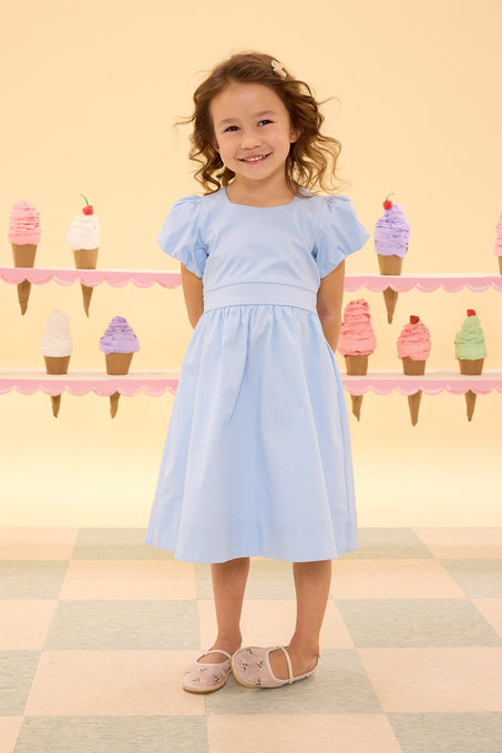 Young girl in a light blue dress standing in front of an ice cream-themed wall.