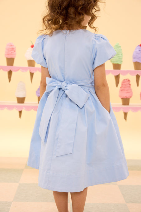 Woman wearing a light blue dress with a belt, standing in front of ice cream cones.