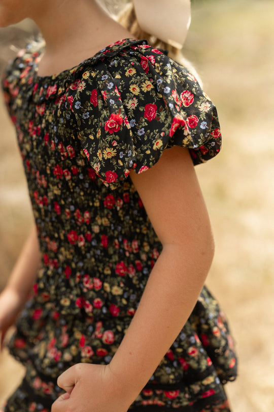 A child wears the Ivy City Co Mini Annalise Top in Obsidian Vintage Poppies, glowing in the sunlight—the perfect choice for picture-perfect Mom and Me matching moments.
