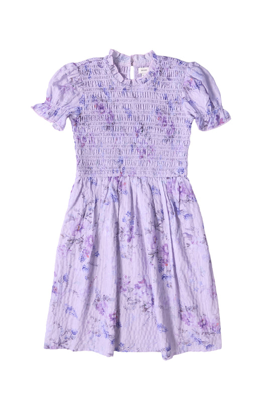 The Mini Flynn Dress in Lavender Aquarelle Fleur by Ivy City Co features a smocked bodice, ruffled collar, and watercolor floral skirt—creating a delicate, airy look perfect for special occasions.