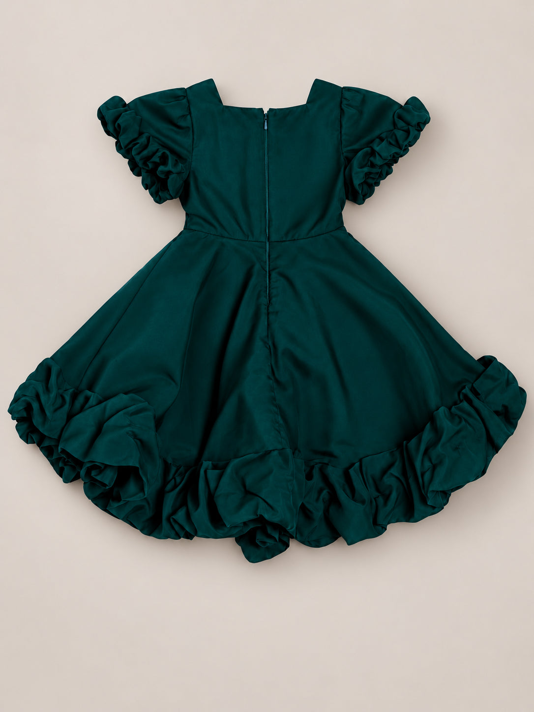 The Mini Kendy Dress in Emerald by Ivy City Co is a girls’ green short-sleeve dress featuring ruffled sleeves, a ruffled hem, and a flared skirt with a back zipper. Displayed flat on a beige background, this dress is perfect for holiday portraits.