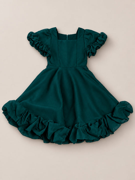 The Mini Kendy Dress in Emerald by Ivy City Co is a holiday portrait dress for young girls, featuring puffed short sleeves, a square neckline, and a ruffled hem, displayed flat on a beige background.