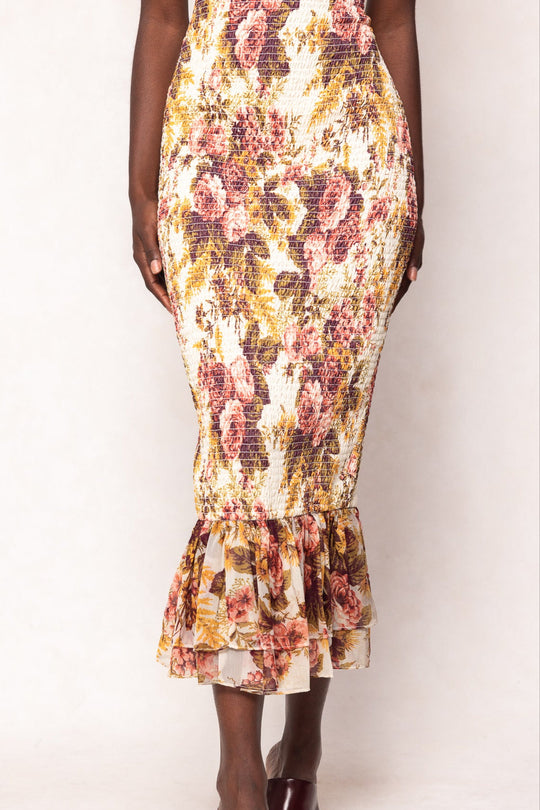 A person wearing the Mira Dress in Garden Rose by Ivy City Co, a fitted skirt adorned with a ruffled hem and covered in pink, yellow, and green floral patterns on a white background; reminiscent of pink rose elegance, only the lower body is visible.