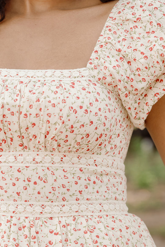 A close-up of a person wearing the Mirabelle Dress in Cream Ditsy Floral by Ivy City Co, featuring short puff sleeves and delicate lace trim at the waist, standing outdoors.