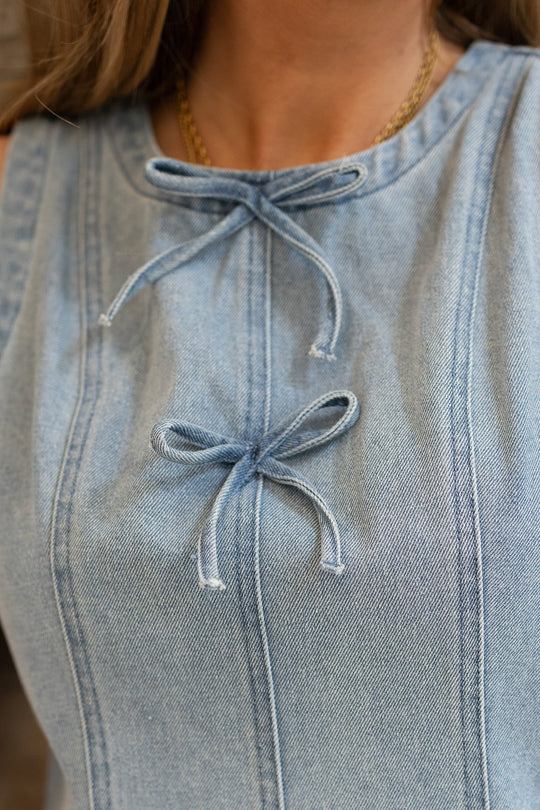 Close-up of a person wearing the Ivy City Co Austin Dress in Light Wash Denim, featuring two tied bows on the front and a visible gold necklace around the neck.