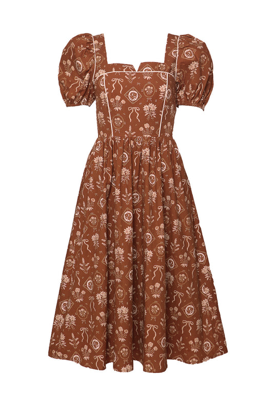 The Nash Dress in Sepia Bows by Ivy City Co is a brown cottagecore midi with puffed short sleeves, square neckline, white floral bow pattern, fitted bodice, and flared skirt for a charming vintage-inspired look.
