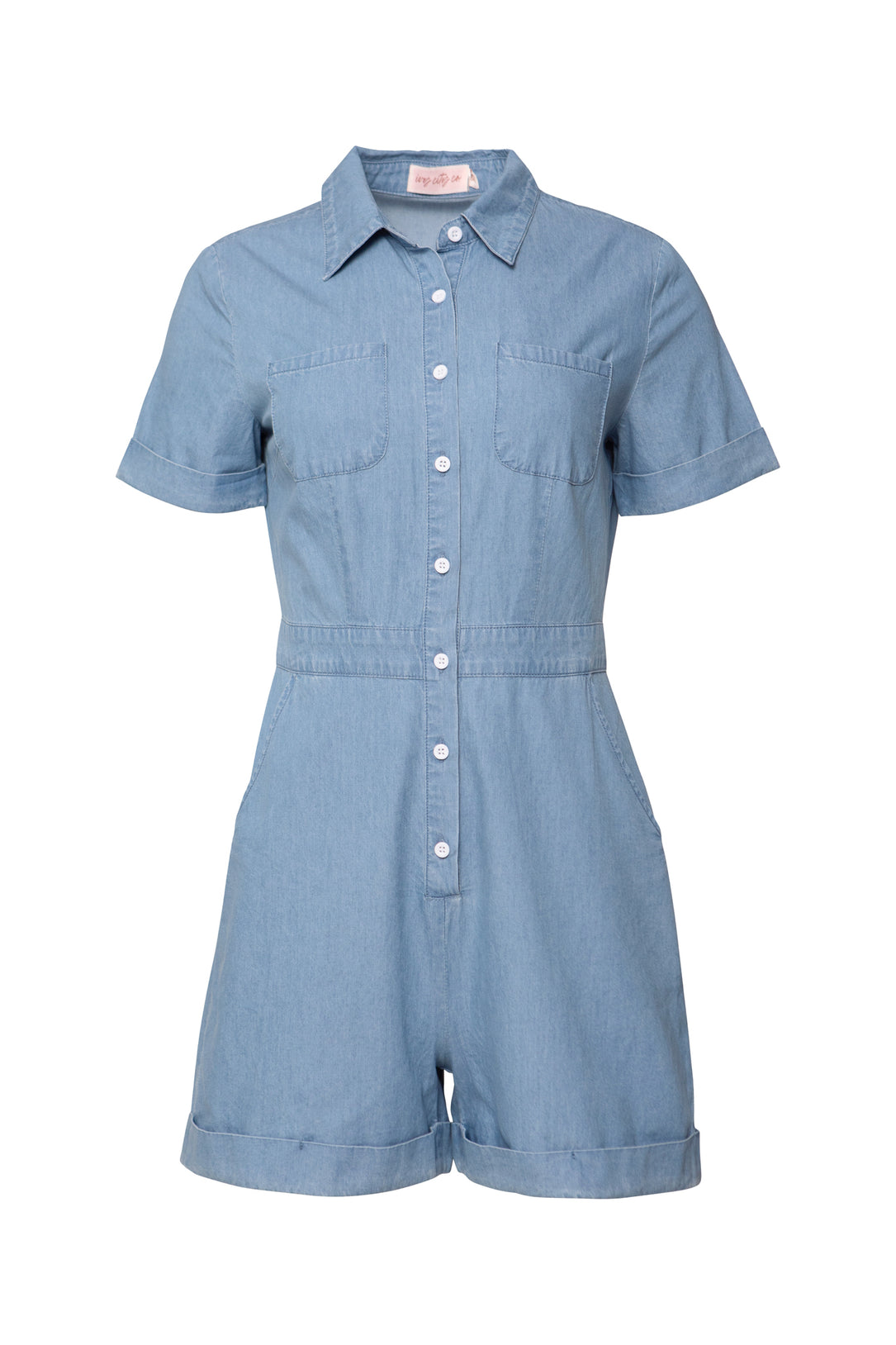 The Natalia Romper in Chambray by Ivy City Co features a light blue design with short sleeves, collar, front button closure (nursing friendly), chest and side pockets, and cuffed shorts.