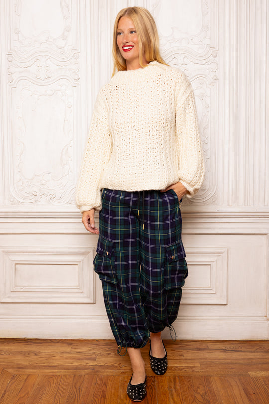Woman wearing a white sweater and plaid pants against a decorative wall.