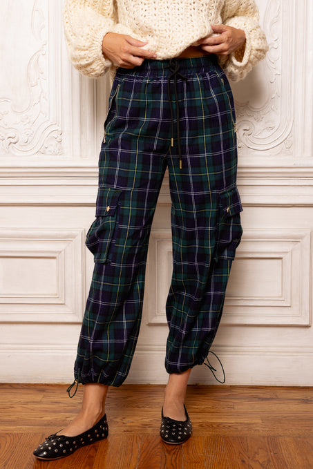 Person wearing plaid pants and a cream sweater against a decorative wall.