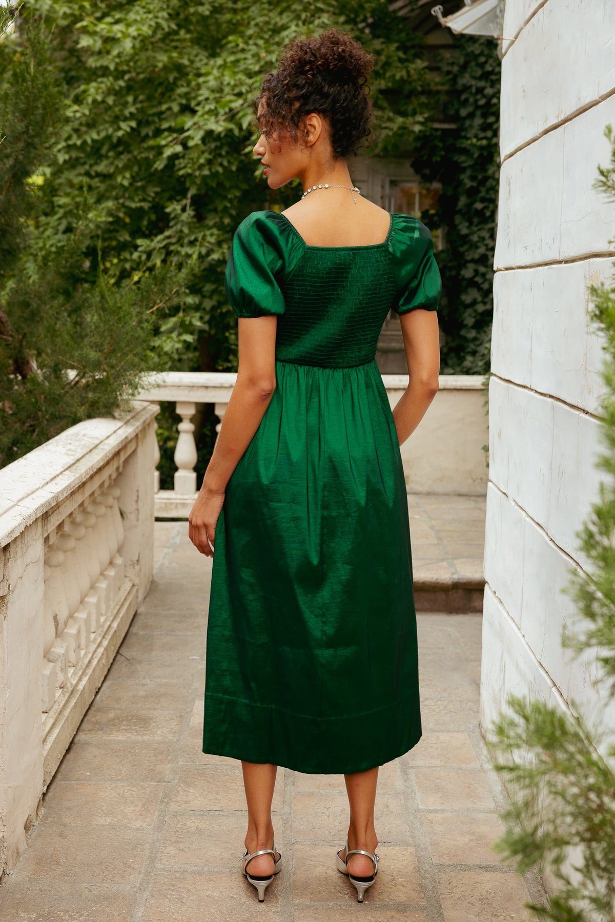 The back view of a person wearing an Ivy City Co Cassie Dress in Green Taffeta, featuring a square neckline, puffed sleeves, and a smocked bodice.